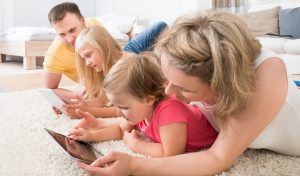 A family laying on the carpet together looking at their tablets and phones